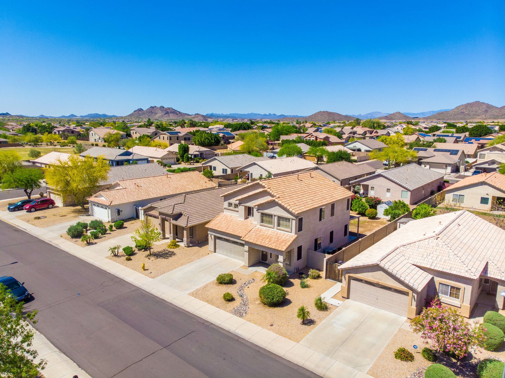 Aerial view of a suburban neighborhood with tan houses, streets, and mountains in the distance