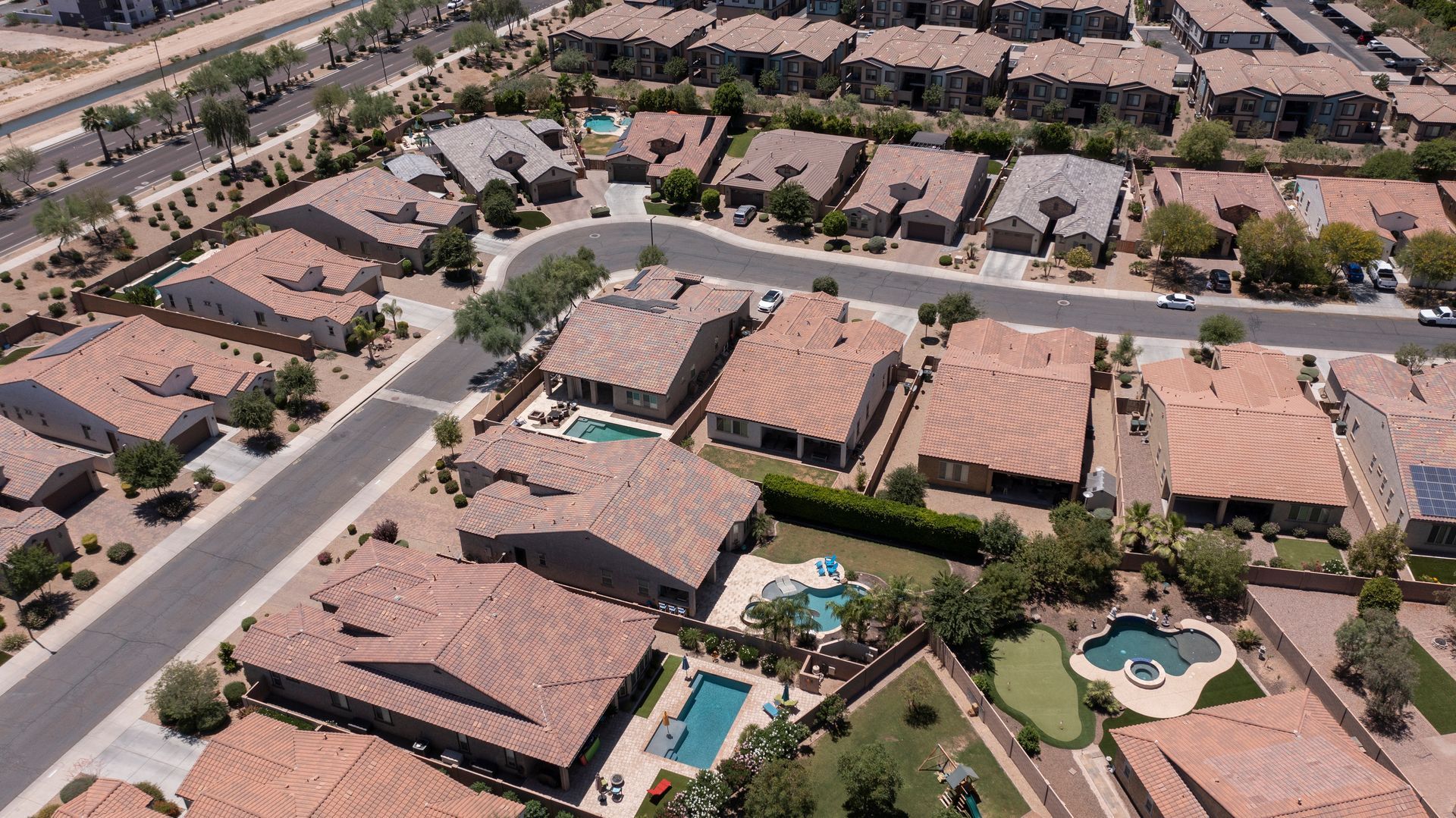 Aerial view of a suburban neighborhood with tan-roofed houses, streets, and two backyard pools Aerial view of a suburban neighborhood with tan-roofed houses, streets, and two backyard pools