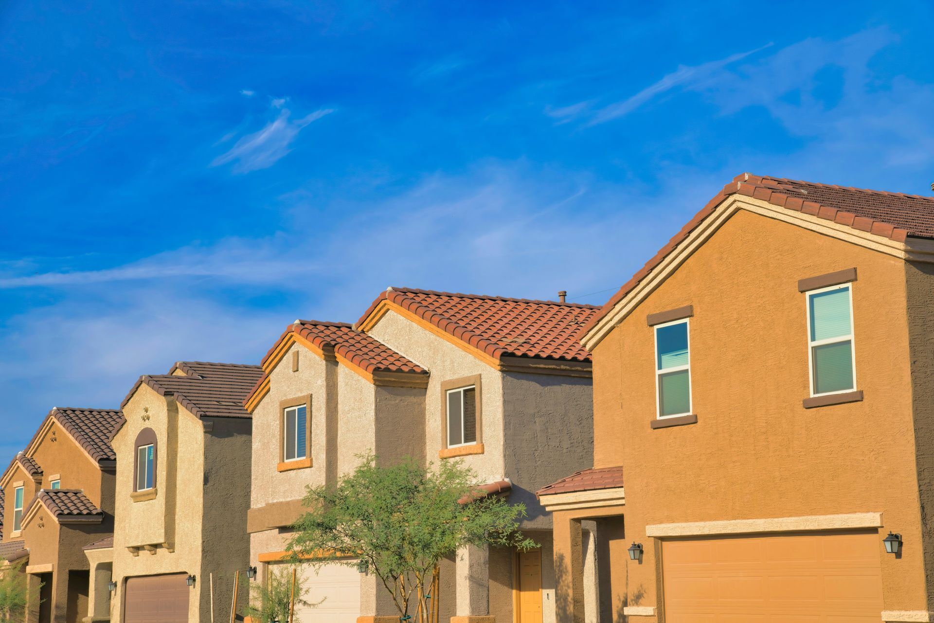 Row of tan stucco suburban houses with red-tiled roofs under a bright blue sky