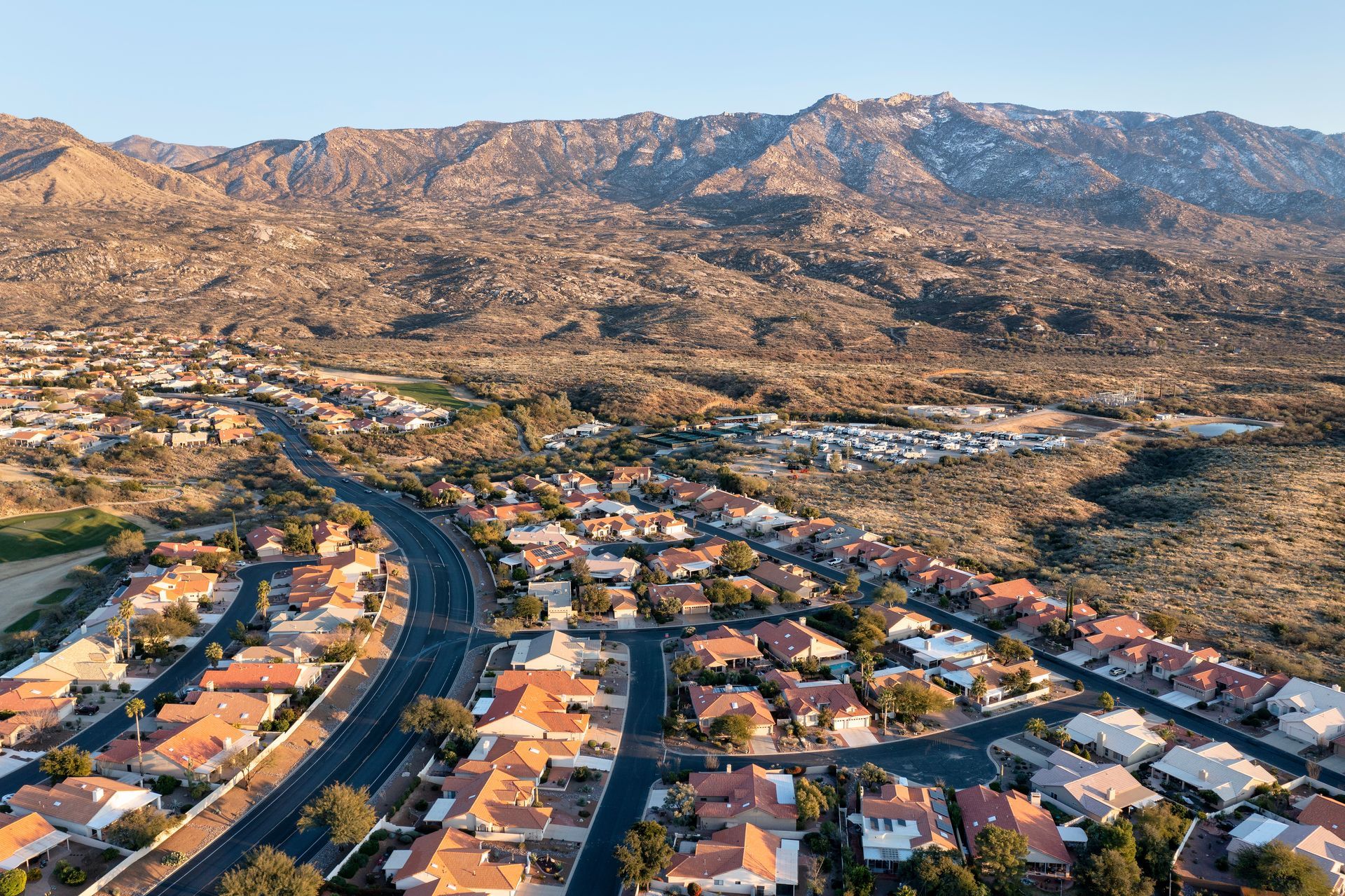 Aerial view of a suburban neighborhood with winding roads, orange roofs, and rocky mountains in the background
