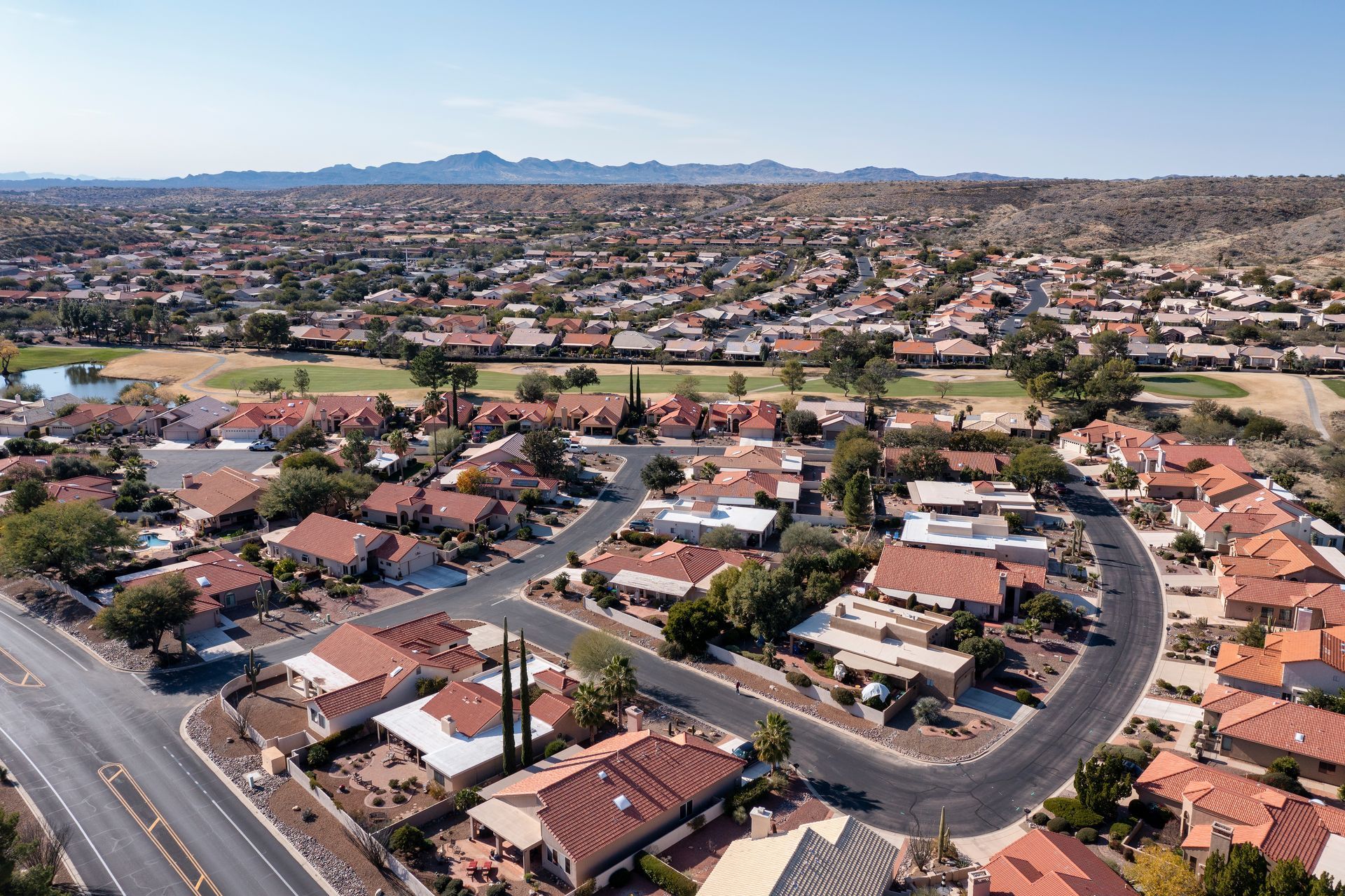 Aerial view of a suburban neighborhood with curving streets, red-roofed houses, and distant hills under a clear sky