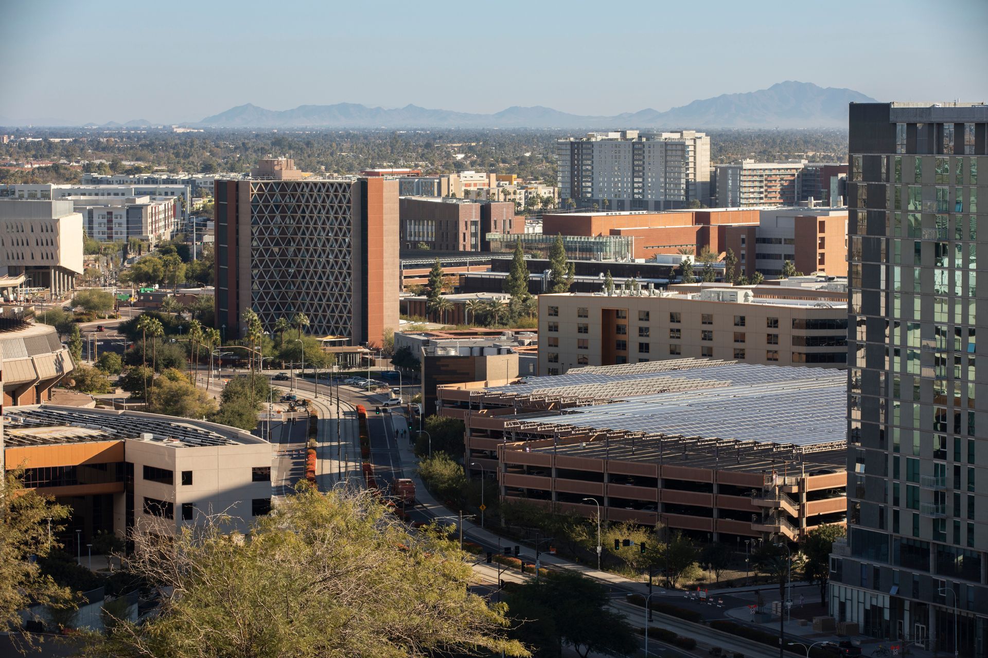 City skyline with mid-rise buildings, mountains in the distance, and a large parking structure in the foreground