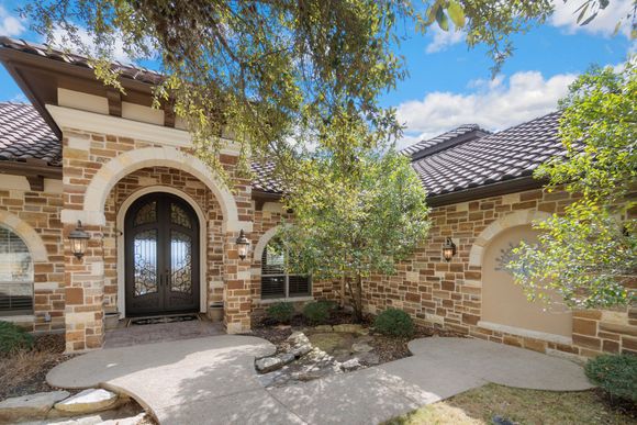 Stone house entry with arched double doors, tiled roof, and a tree shading the front walkway Stone house entry with arched double doors, tiled roof, and a tree shading the front walkway