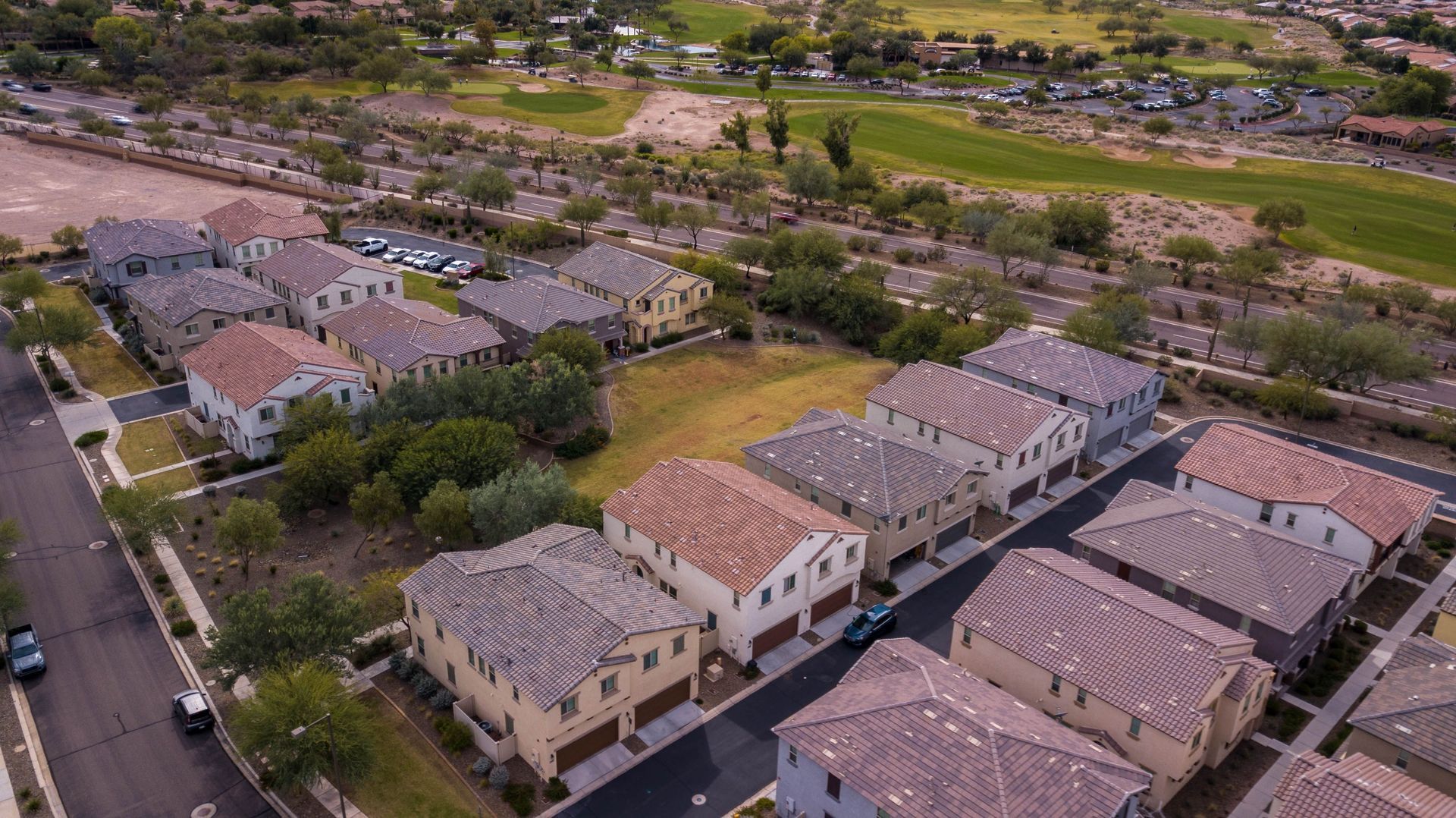 Aerial view of a suburban neighborhood with rows of beige houses, streets, and green trees