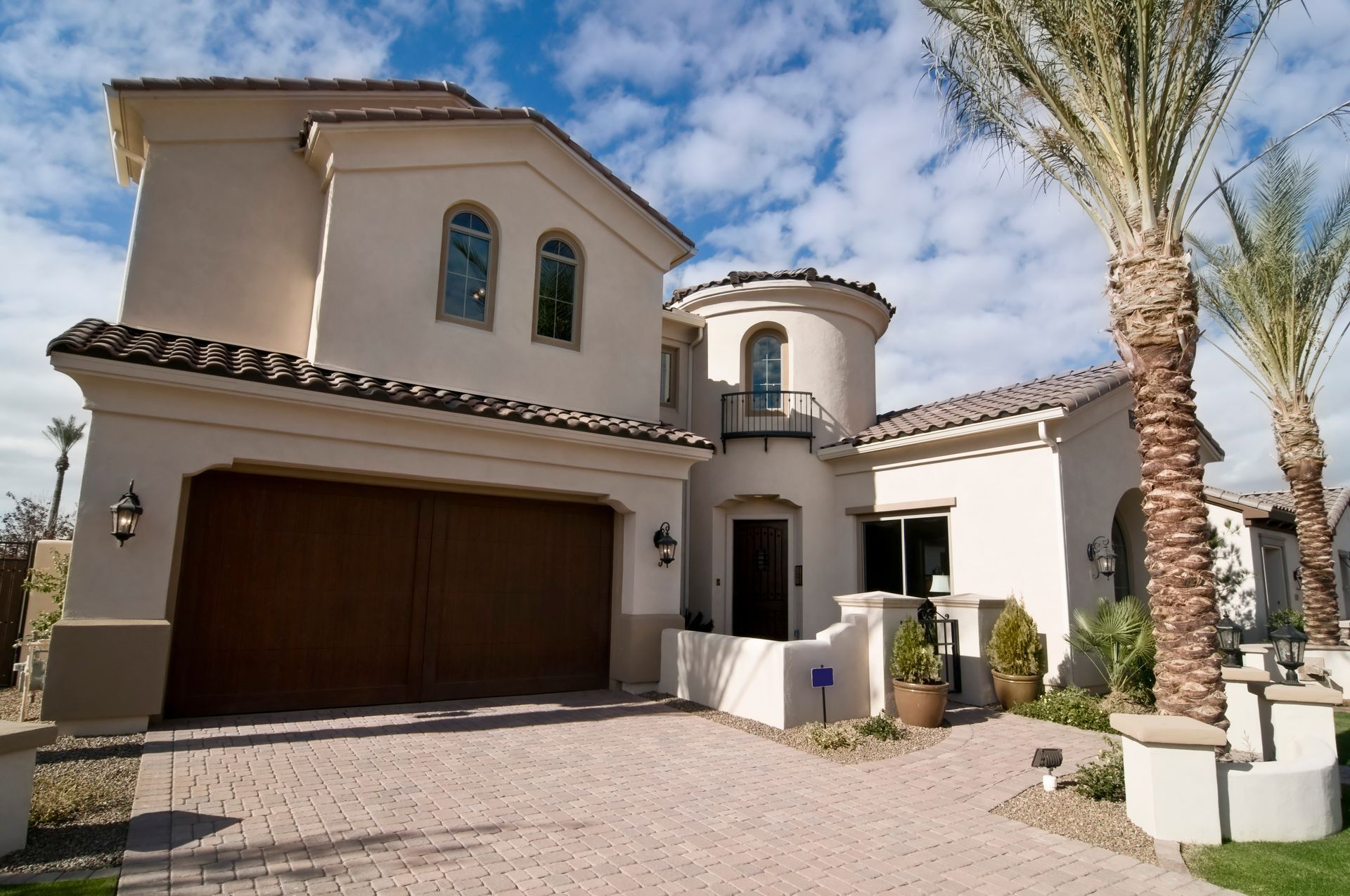 Luxury stucco house exterior with garage, palm trees, and a clear blue sky