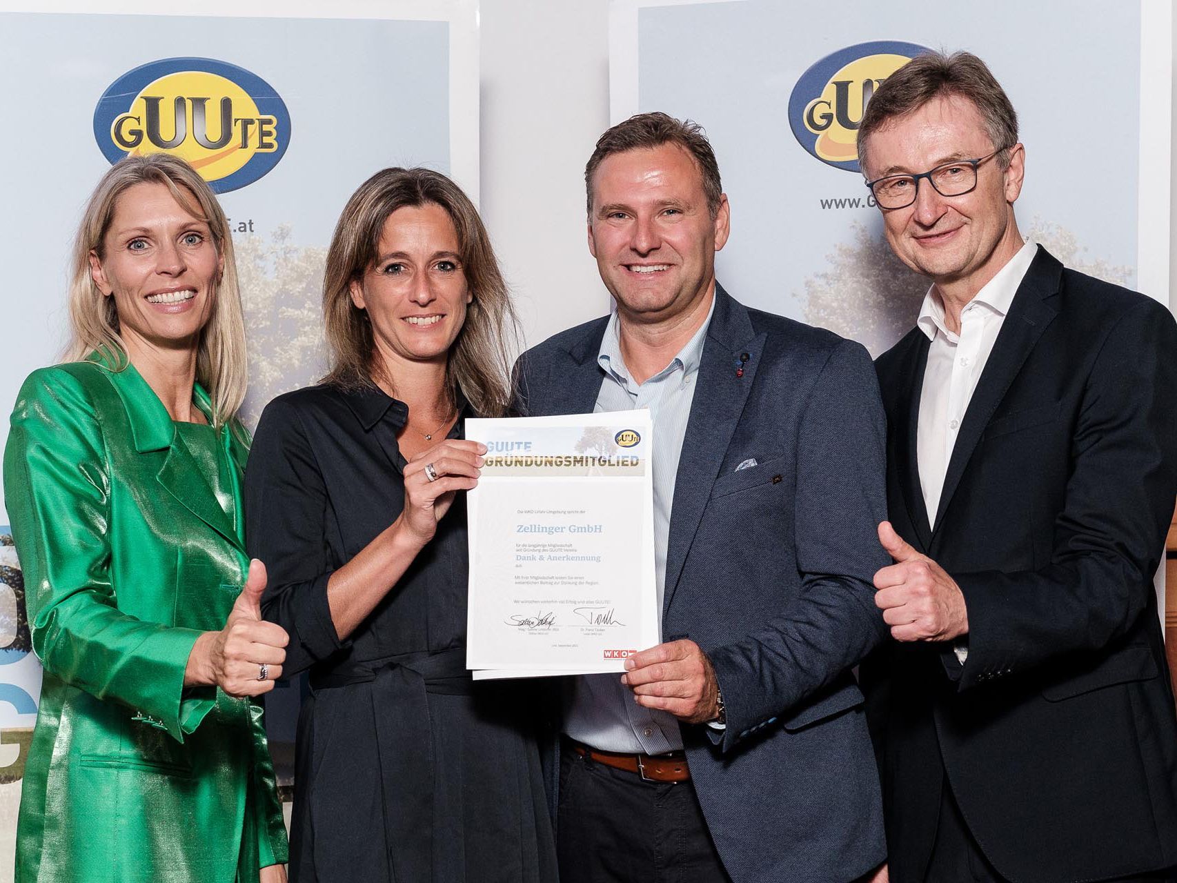 Four people holding a certificate, smiling. Two women and two men in an office setting.