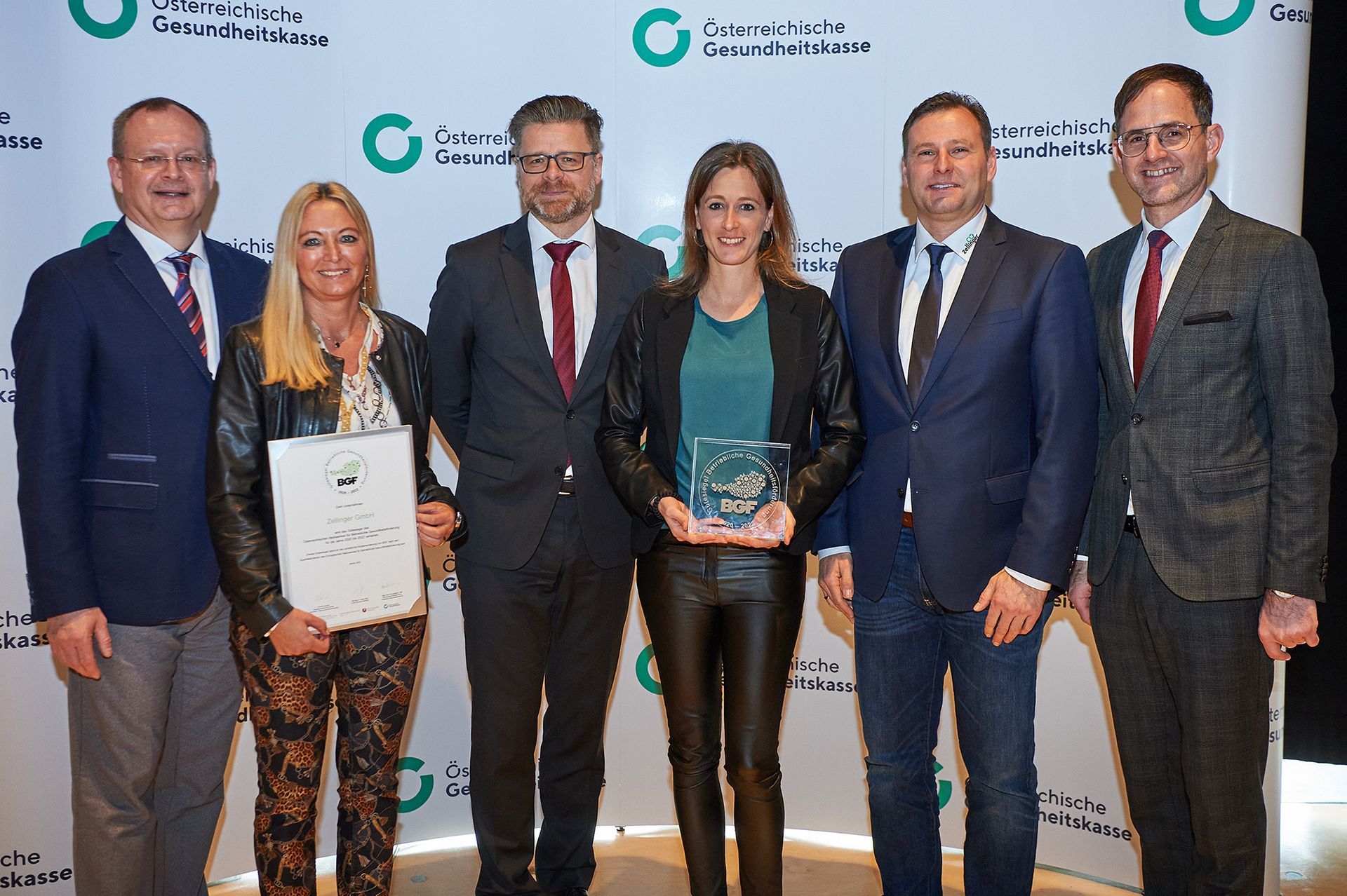 Group of six people, two women and four men, posing with an award in front of a backdrop.