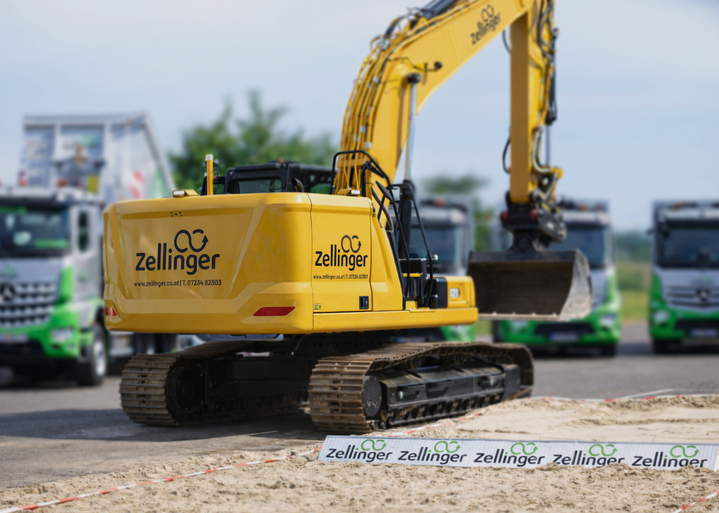Excavator digging earth in a construction site; brown soil and green background with trees.