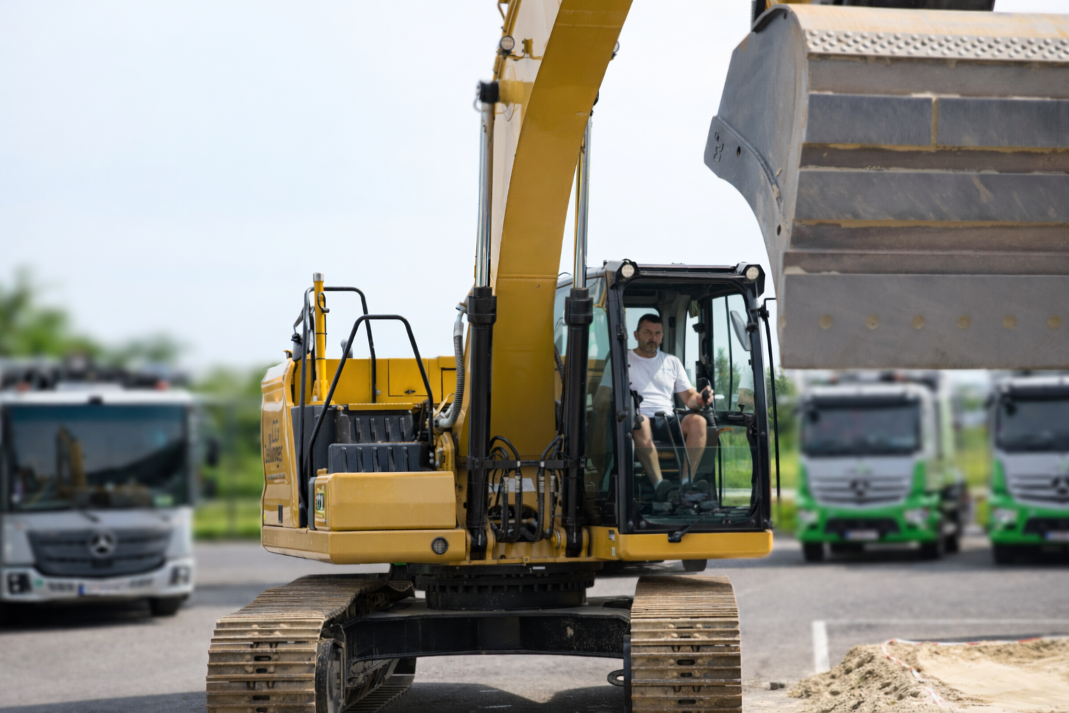 Excavator digging into a hillside, scooping dirt. Gray machine with black details, outdoors in a wooded area.