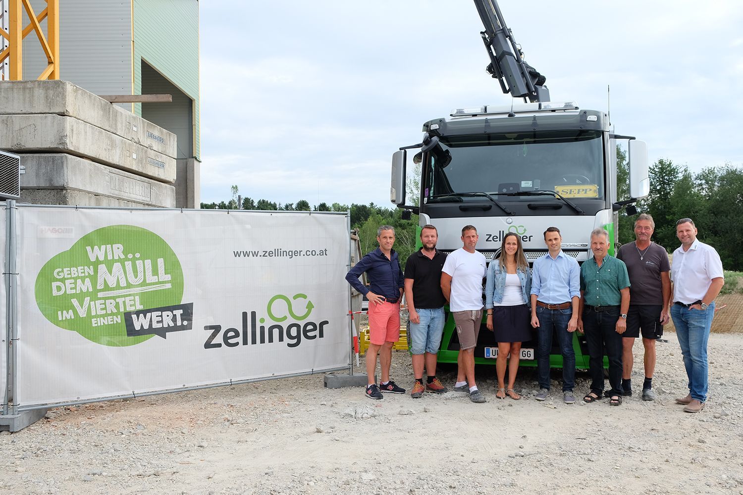 Group of people pose in front of a truck and a sign that says