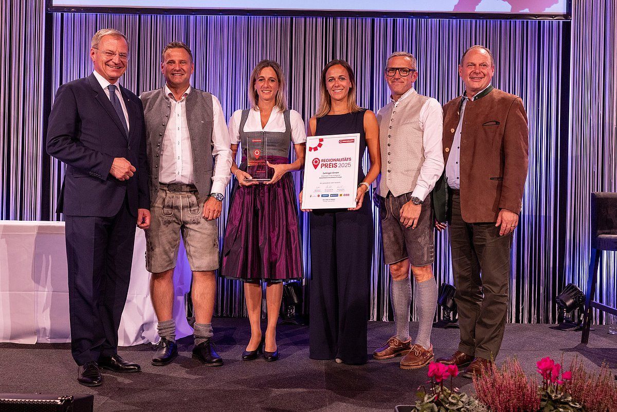 Group of people on stage holding an award and a certificate; formal and traditional attire.