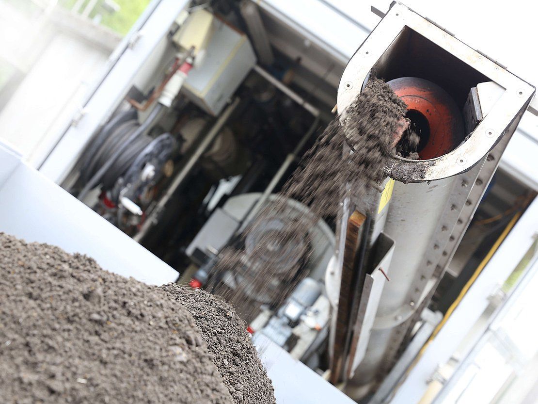 Machine dispensing soil; gray, metallic structure; close-up; outdoor setting.