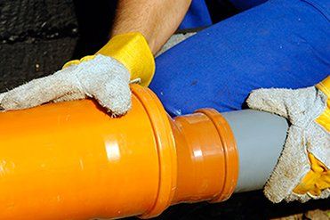 Un hombre que lleva guantes amarillos está trabajando en una tubería.