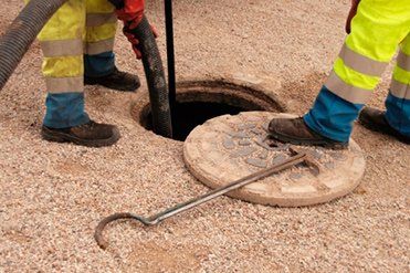 Dos hombres están limpiando una alcantarilla con una manguera de vacío.
