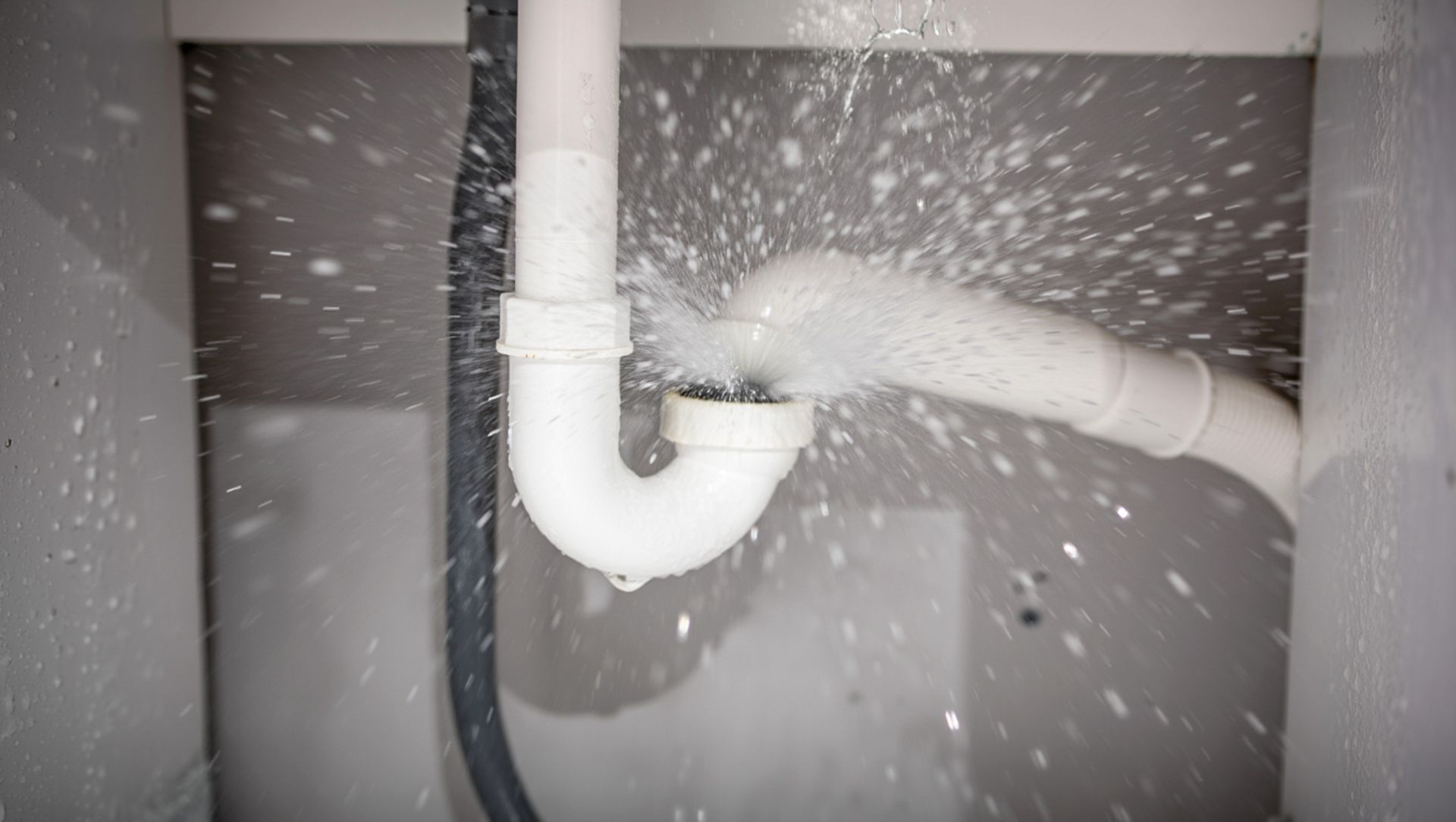 Burst plumbing pipe spraying water under a sink, showing active leak and urgent damage.