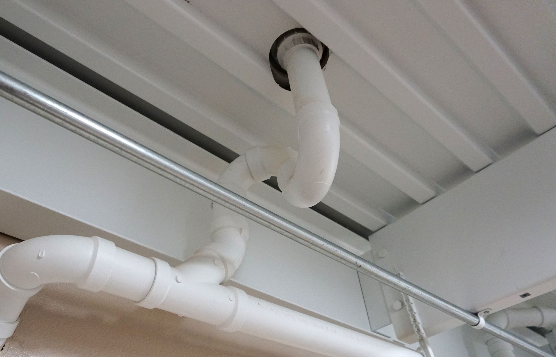 White PVC plumbing pipes attached to a white ceiling.