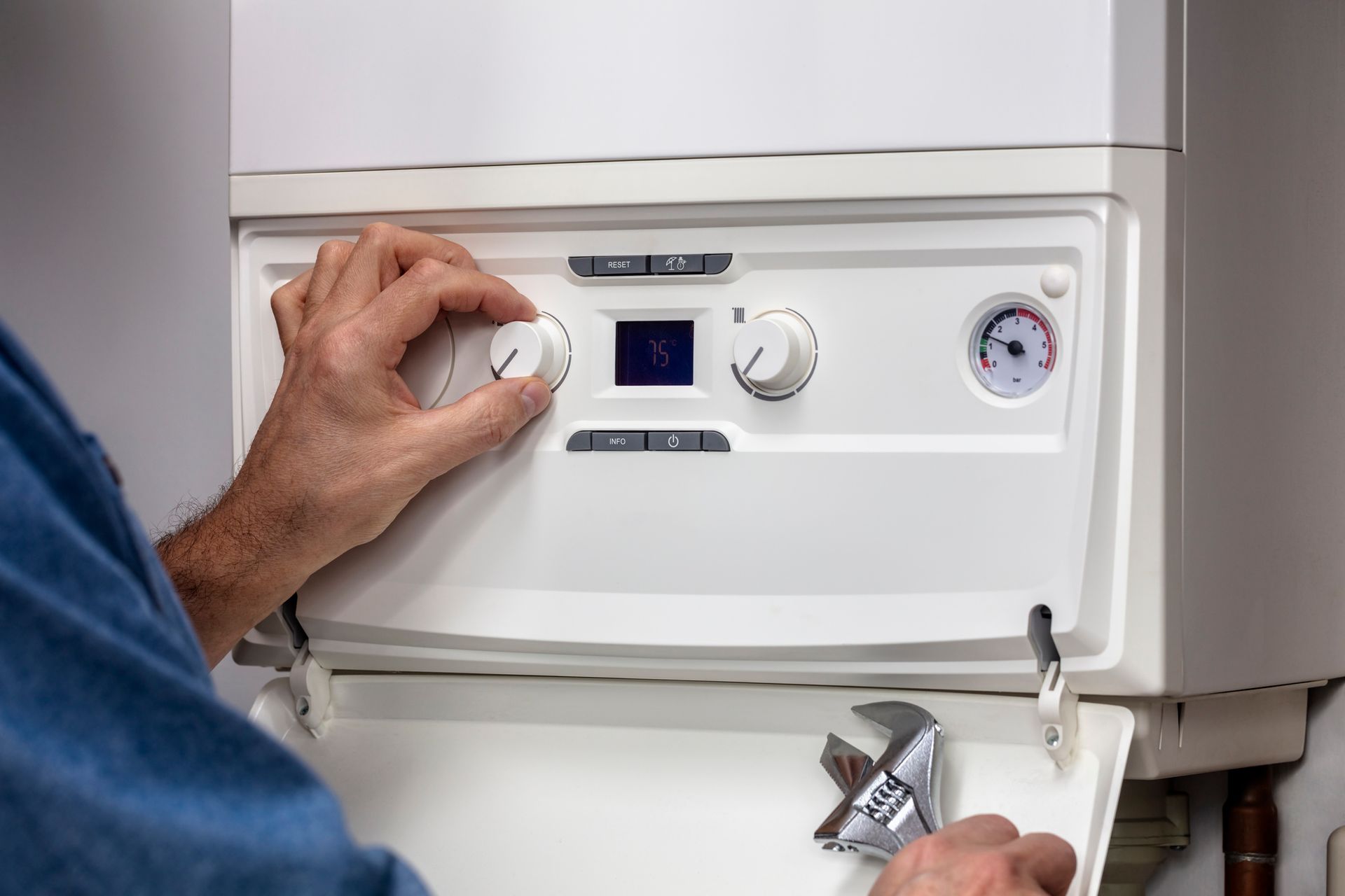 Person adjusting a white boiler with a wrench, focusing on controls.