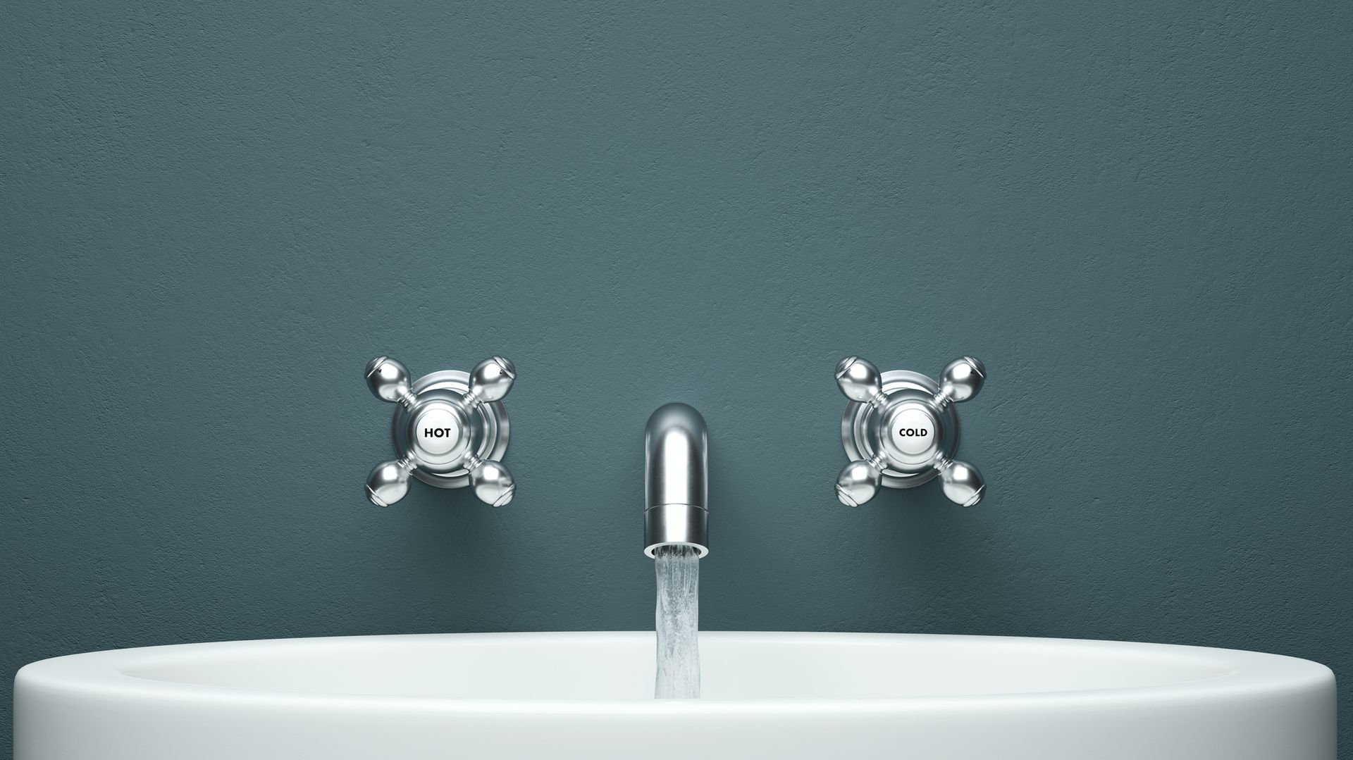 Silver faucet with running water above a white sink, against a teal wall.