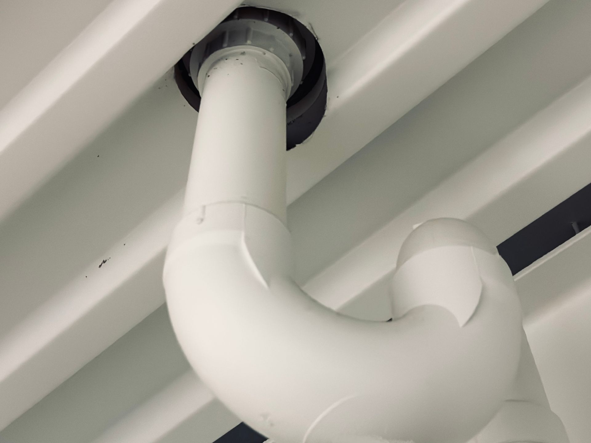White PVC pipe curves through a white ceiling.