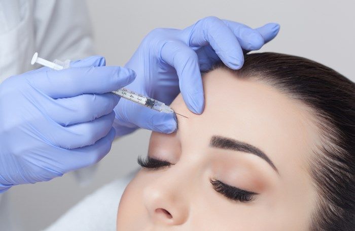 A woman is getting a botox injection in her forehead.