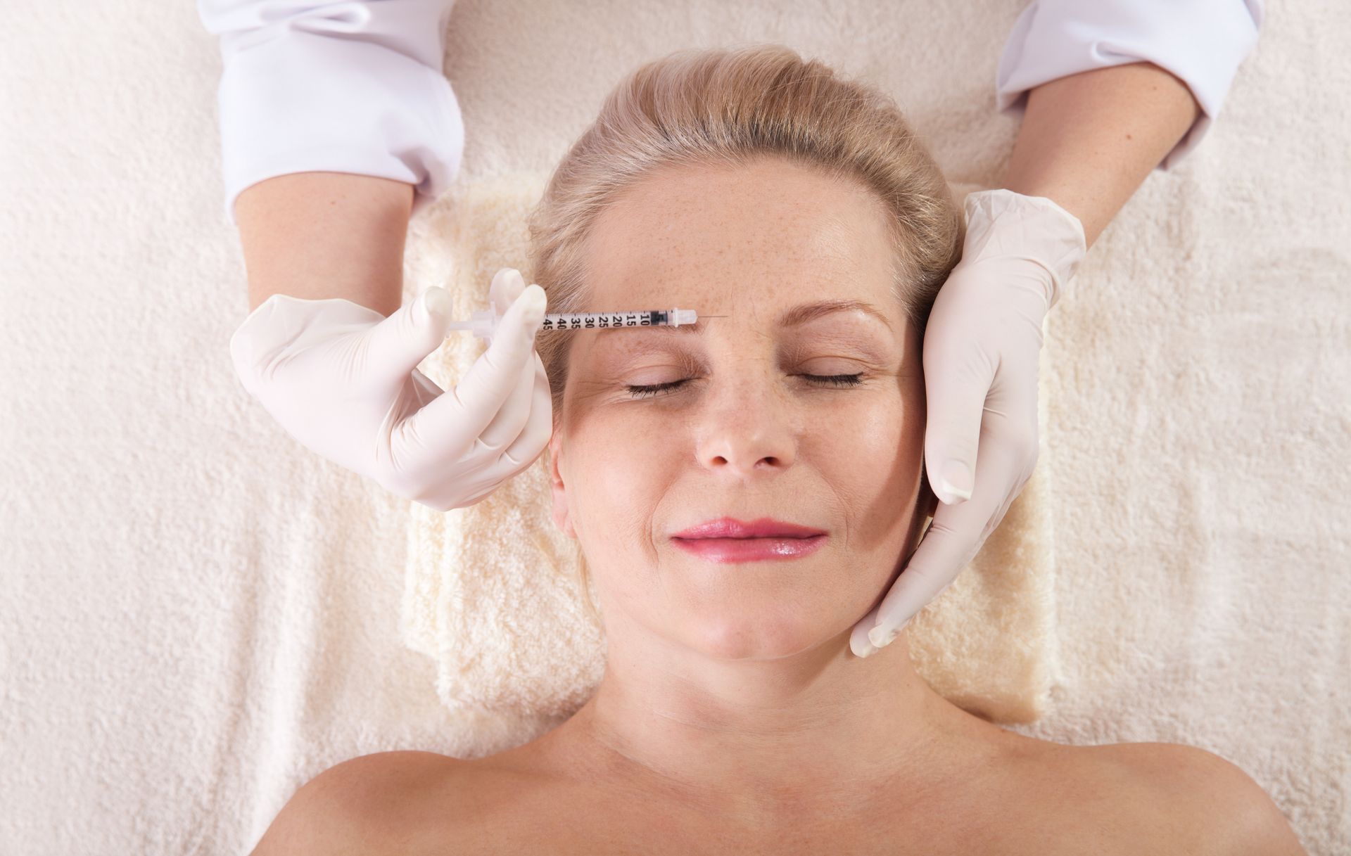 A woman is getting a botox injection in her forehead.