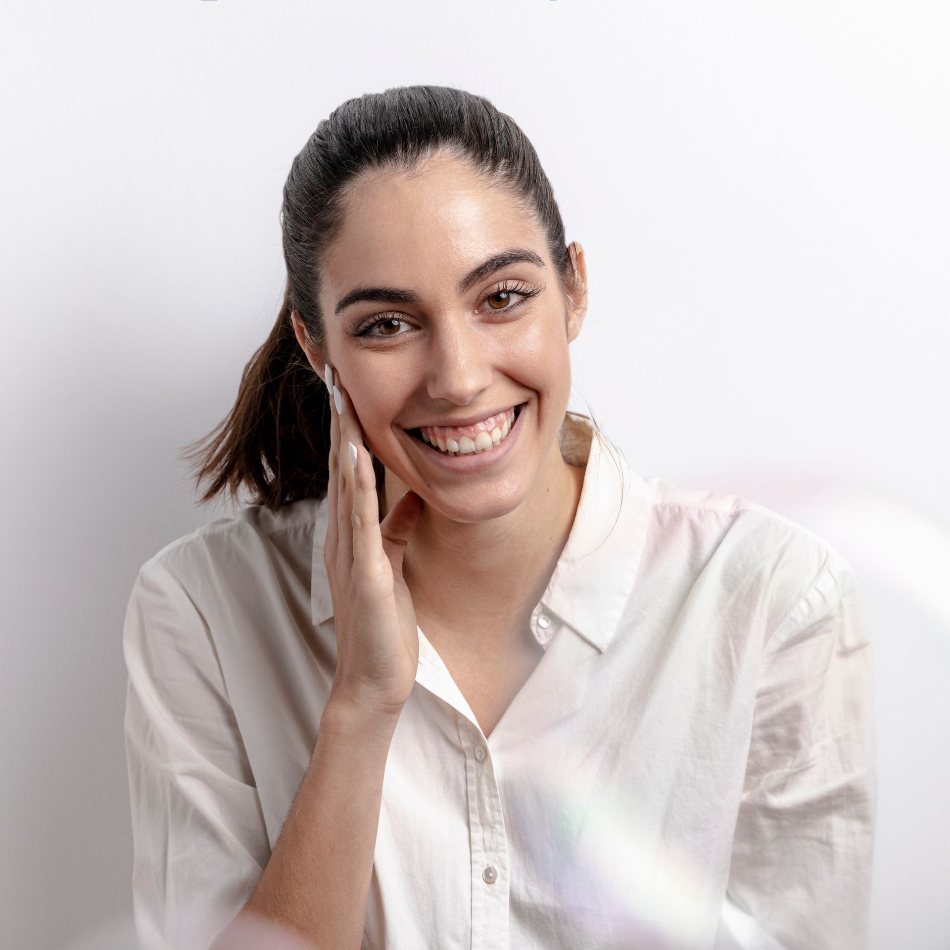 a woman in a white shirt is smiling and touching her face .