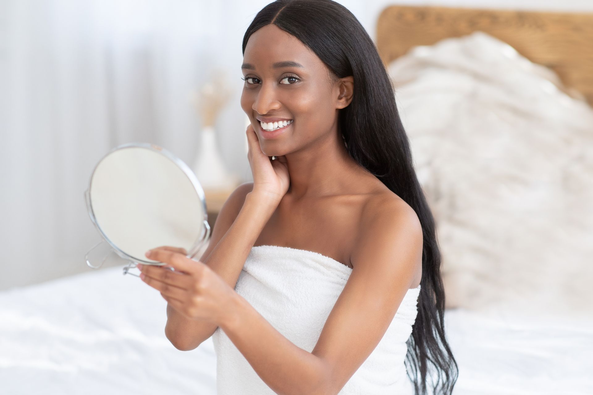 A woman wrapped in a towel is looking at her face in a mirror.