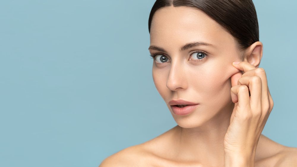 A woman is touching her face with her hand and looking at the camera.