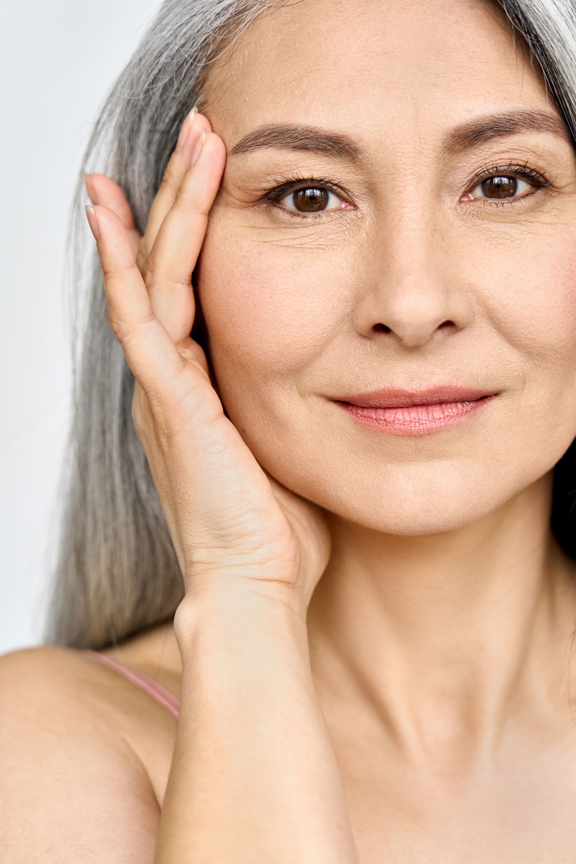 a woman with gray hair is touching her face with her hand and smiling .