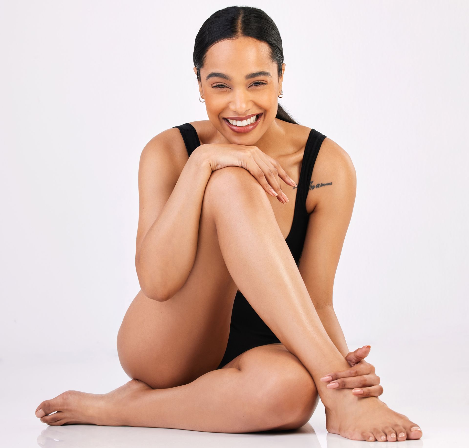 a woman in a black swimsuit is sitting on the floor with her legs crossed and smiling .