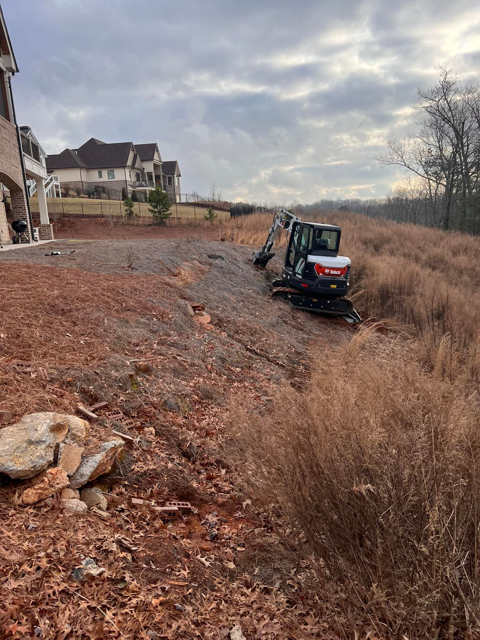 An excavator is sitting in a field next to a house.