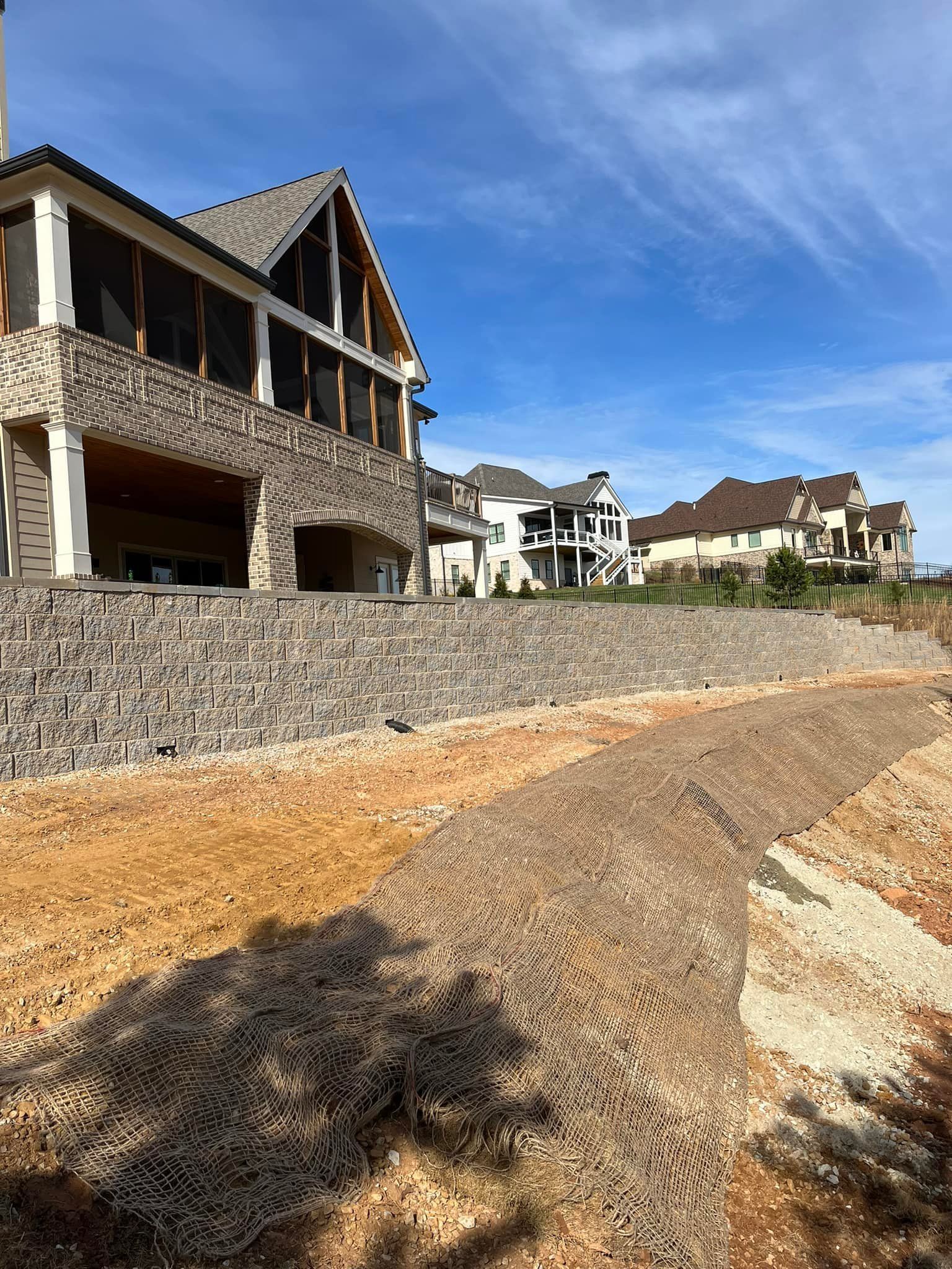 A large house is sitting on top of a hill next to a stone wall.
