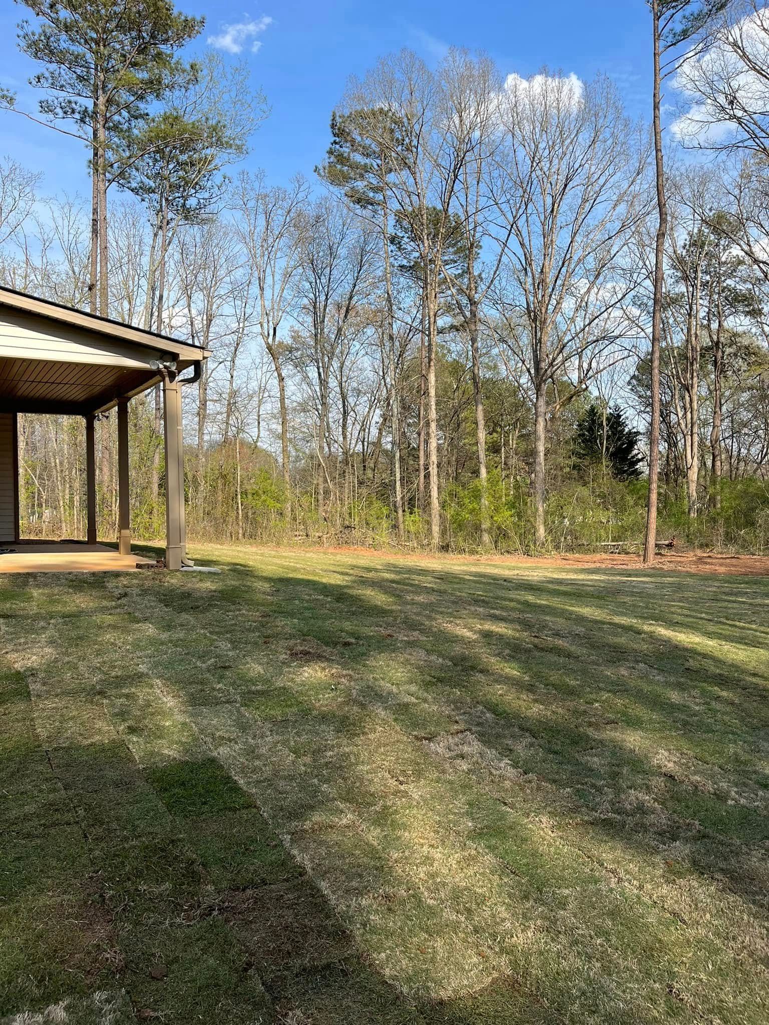 A house with a porch in the middle of a field surrounded by trees.