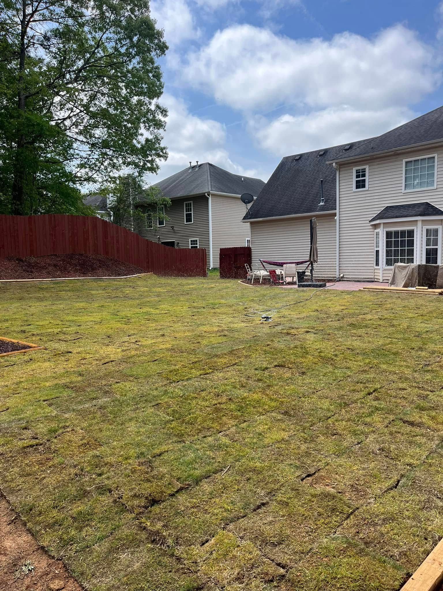 A large lawn in front of a house with a red fence.