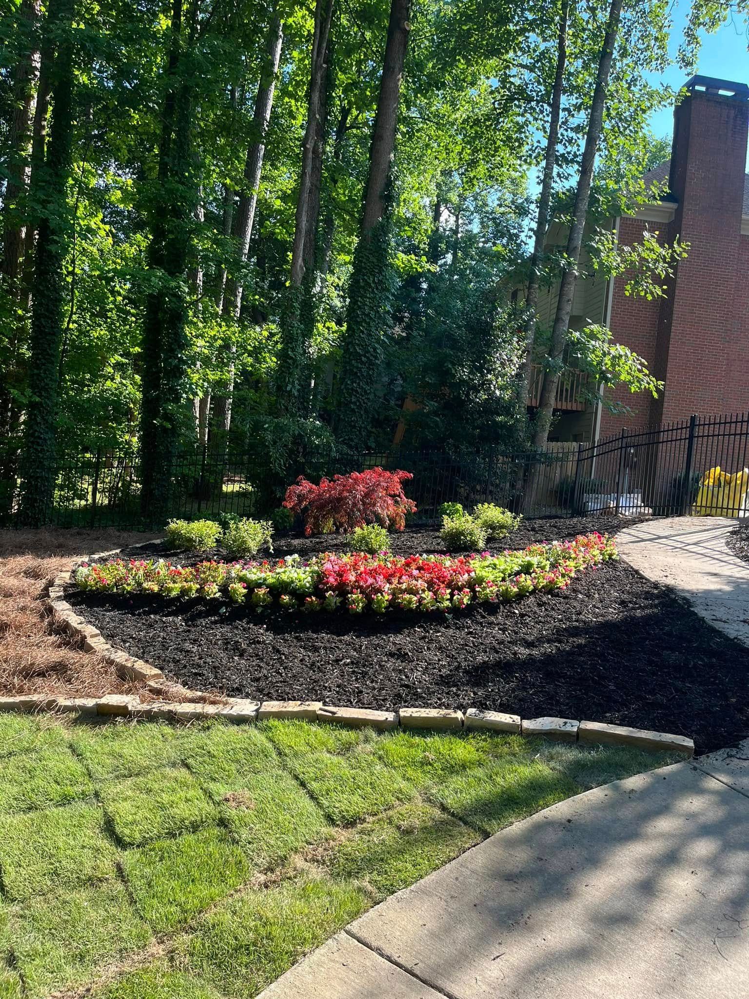 A garden with flowers and mulch in front of a brick house.