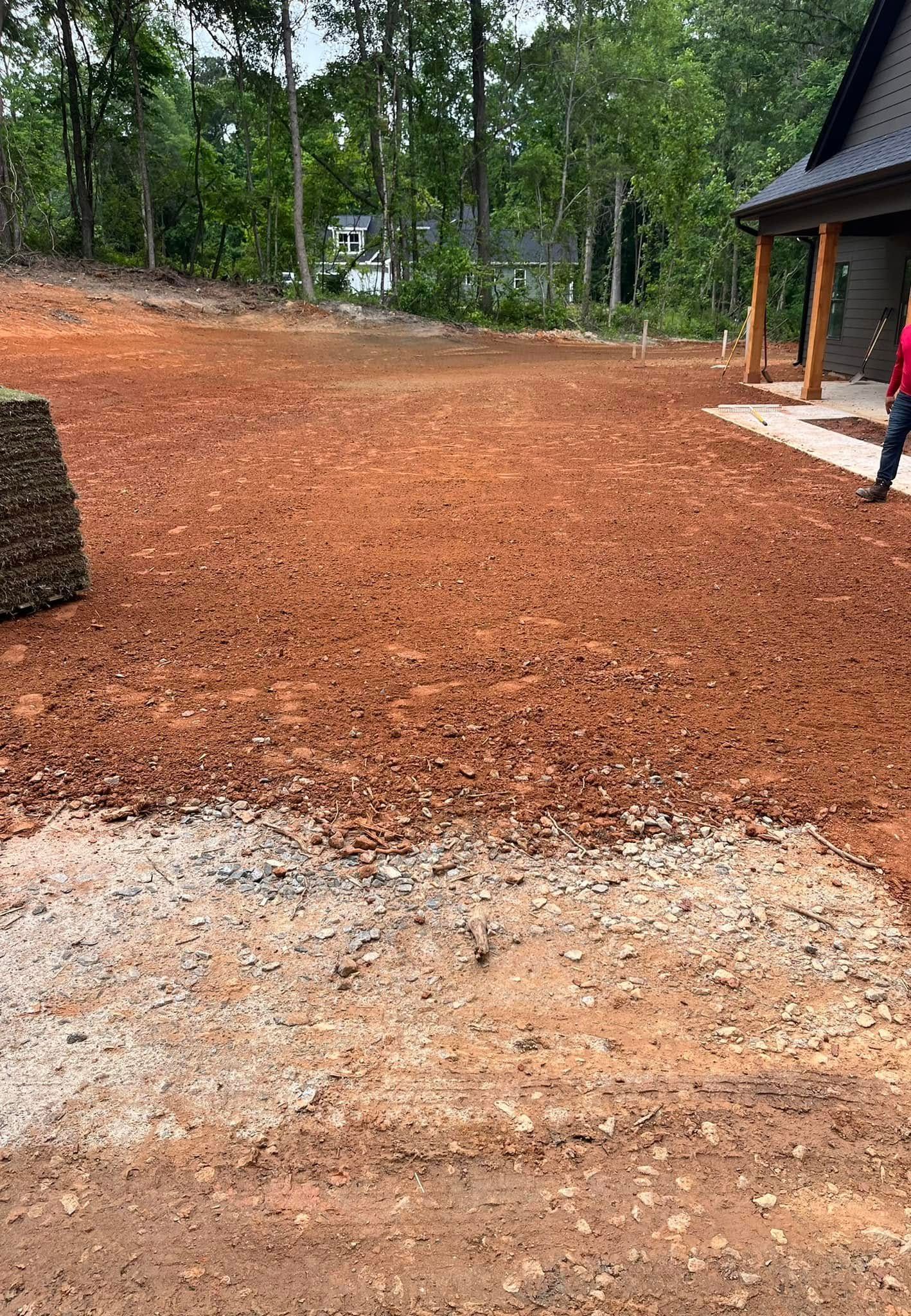 A person is walking through a dirt field in front of a house.