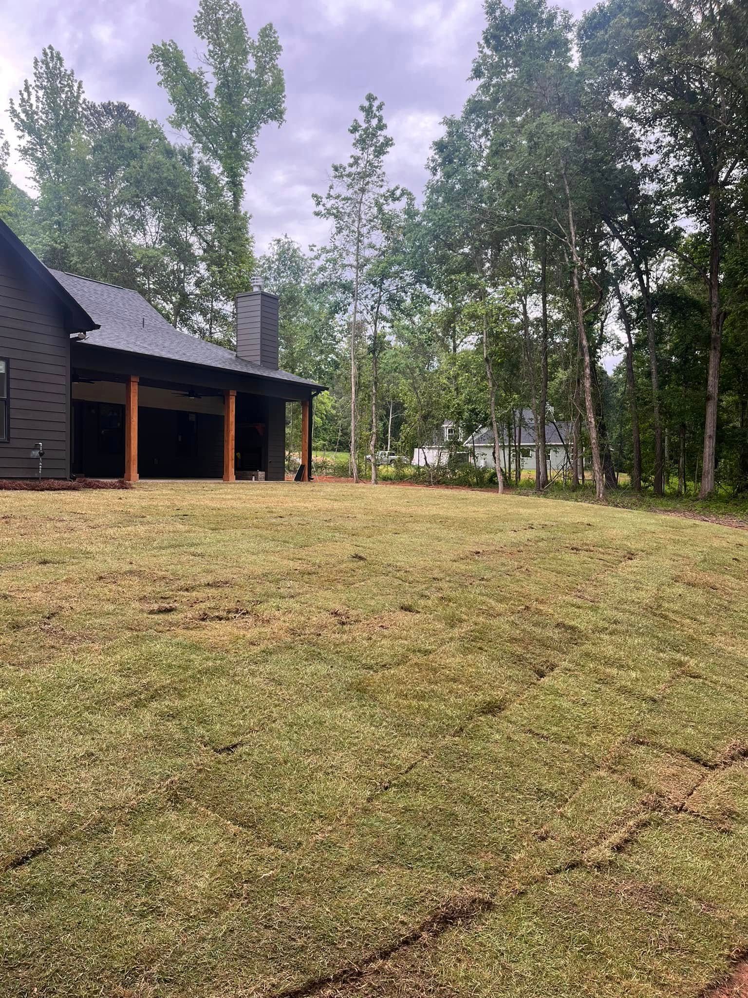 A house is sitting on top of a lush green field surrounded by trees.
