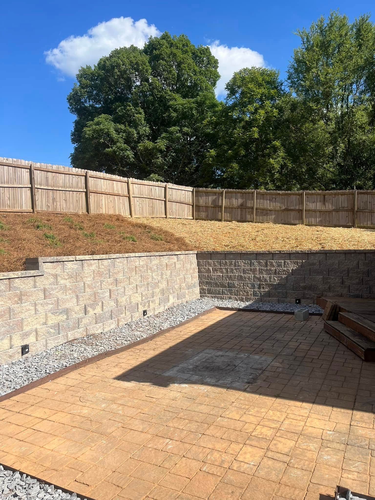 A brick patio with a wooden fence in the background and trees in the background.