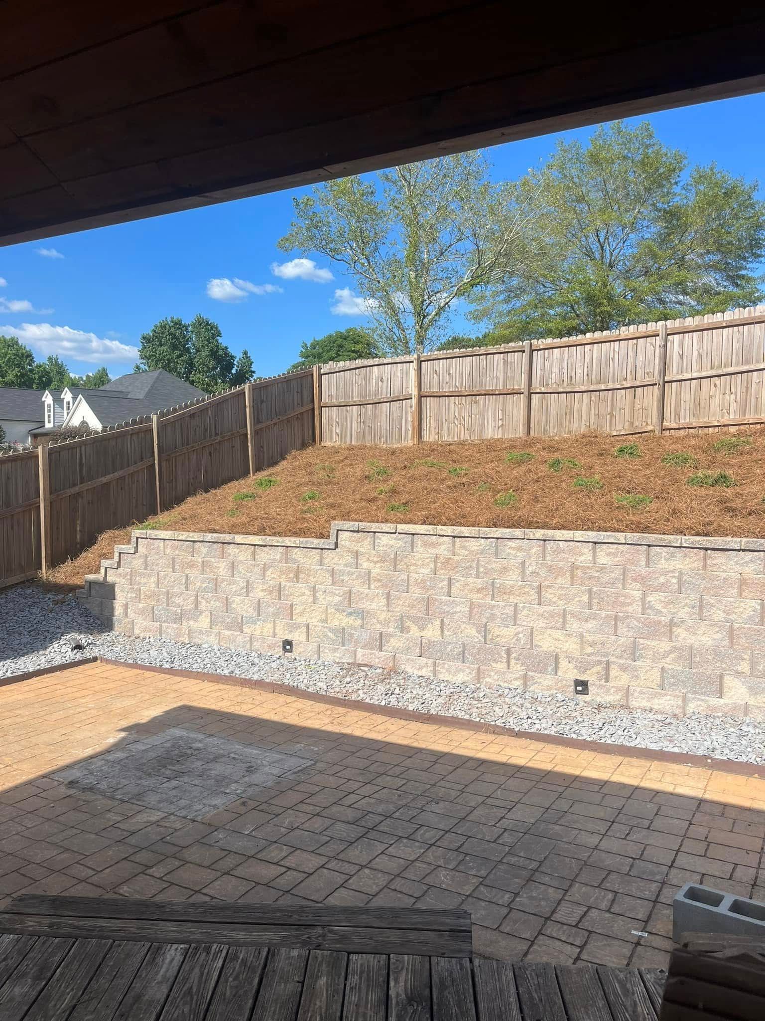 A view of a backyard with a brick wall and a wooden fence.