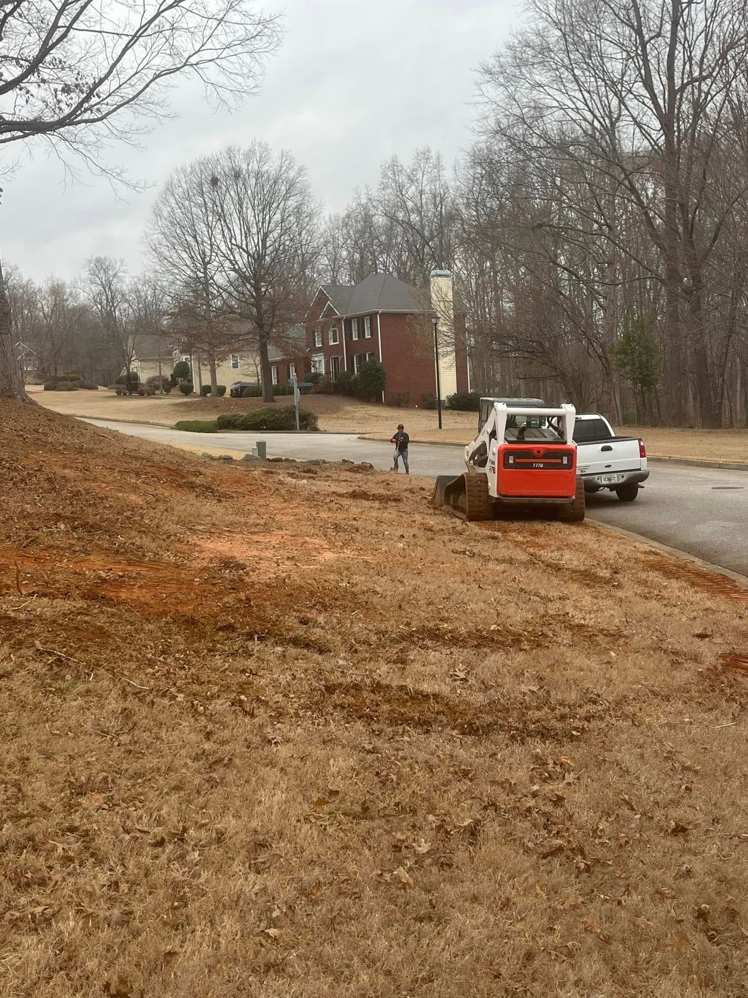 A bulldozer is driving down a dirt road next to a house.