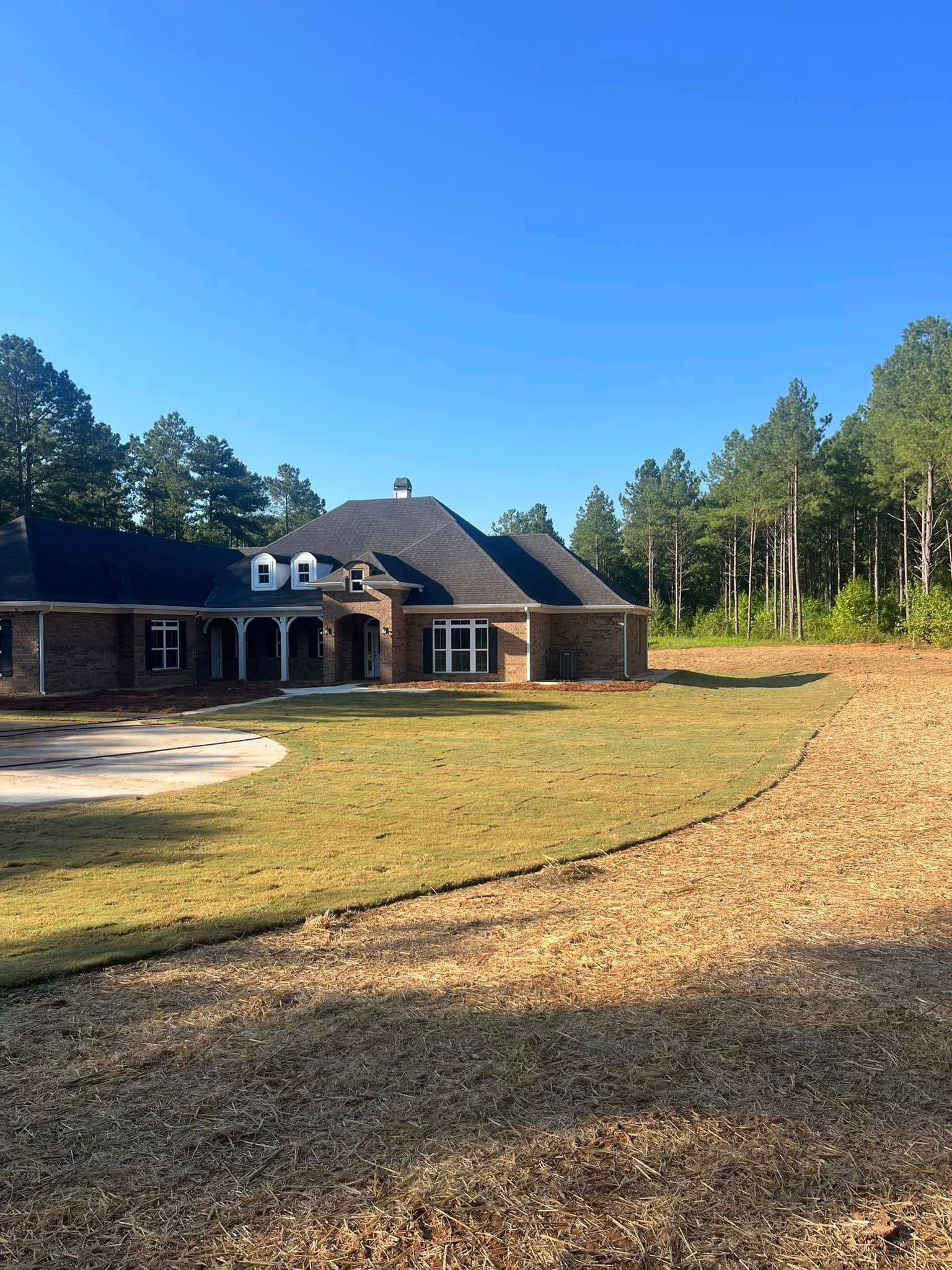 A large house is sitting on top of a lush green field surrounded by trees.