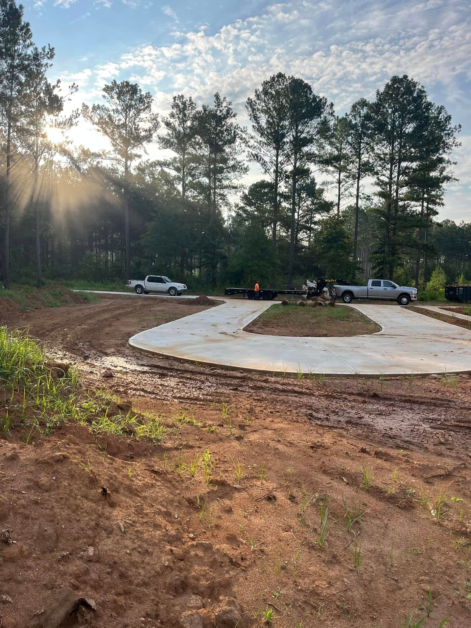 A concrete driveway is being built in the middle of a dirt field surrounded by trees.