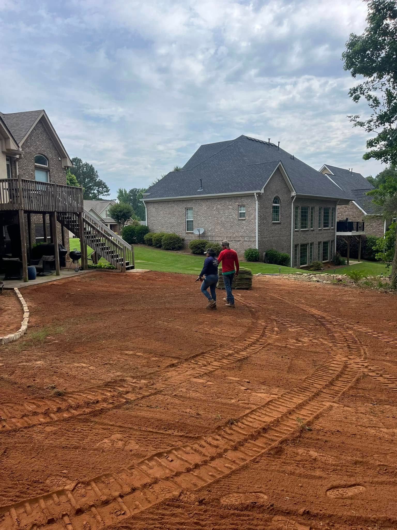 Two men are walking down a dirt road in front of a house.