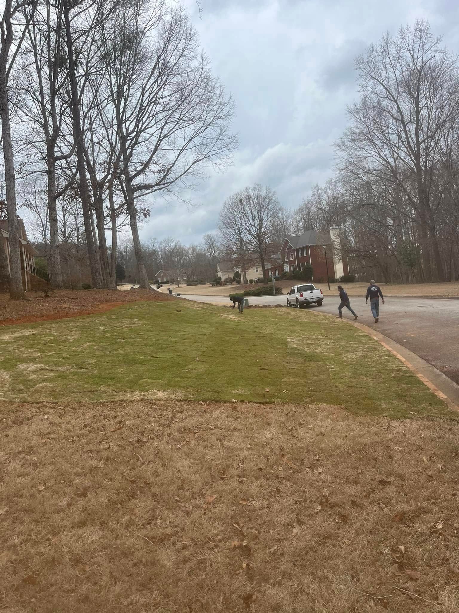 A couple of people are walking down a sidewalk next to a grassy field.