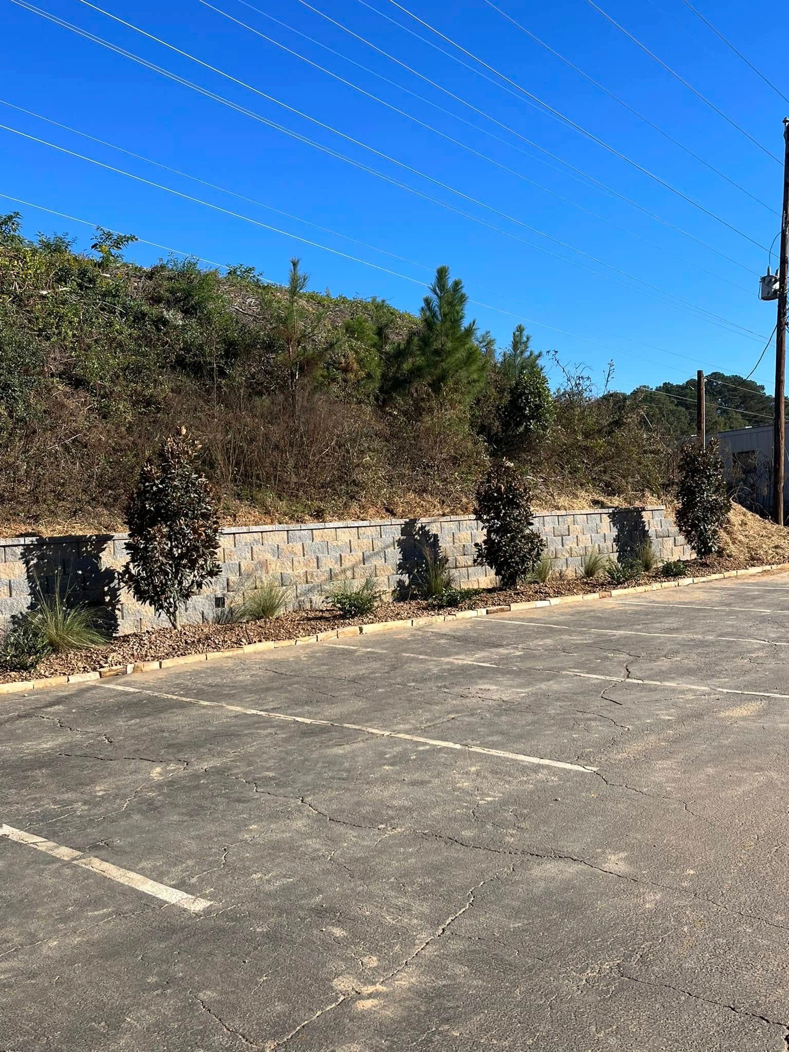 A parking lot with a stone wall and trees in the background on a sunny day.