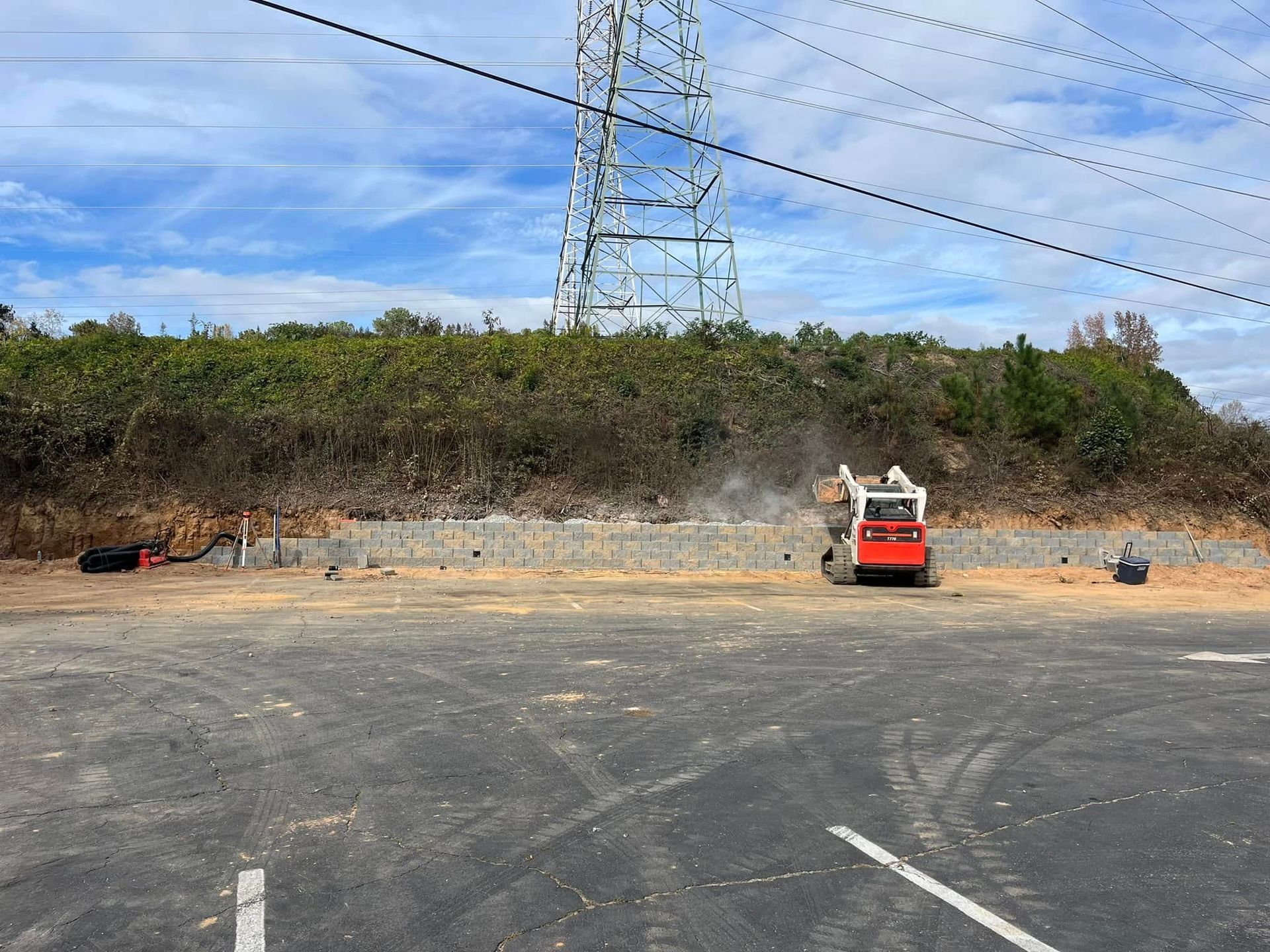 A construction vehicle is parked in a parking lot next to a power tower.
