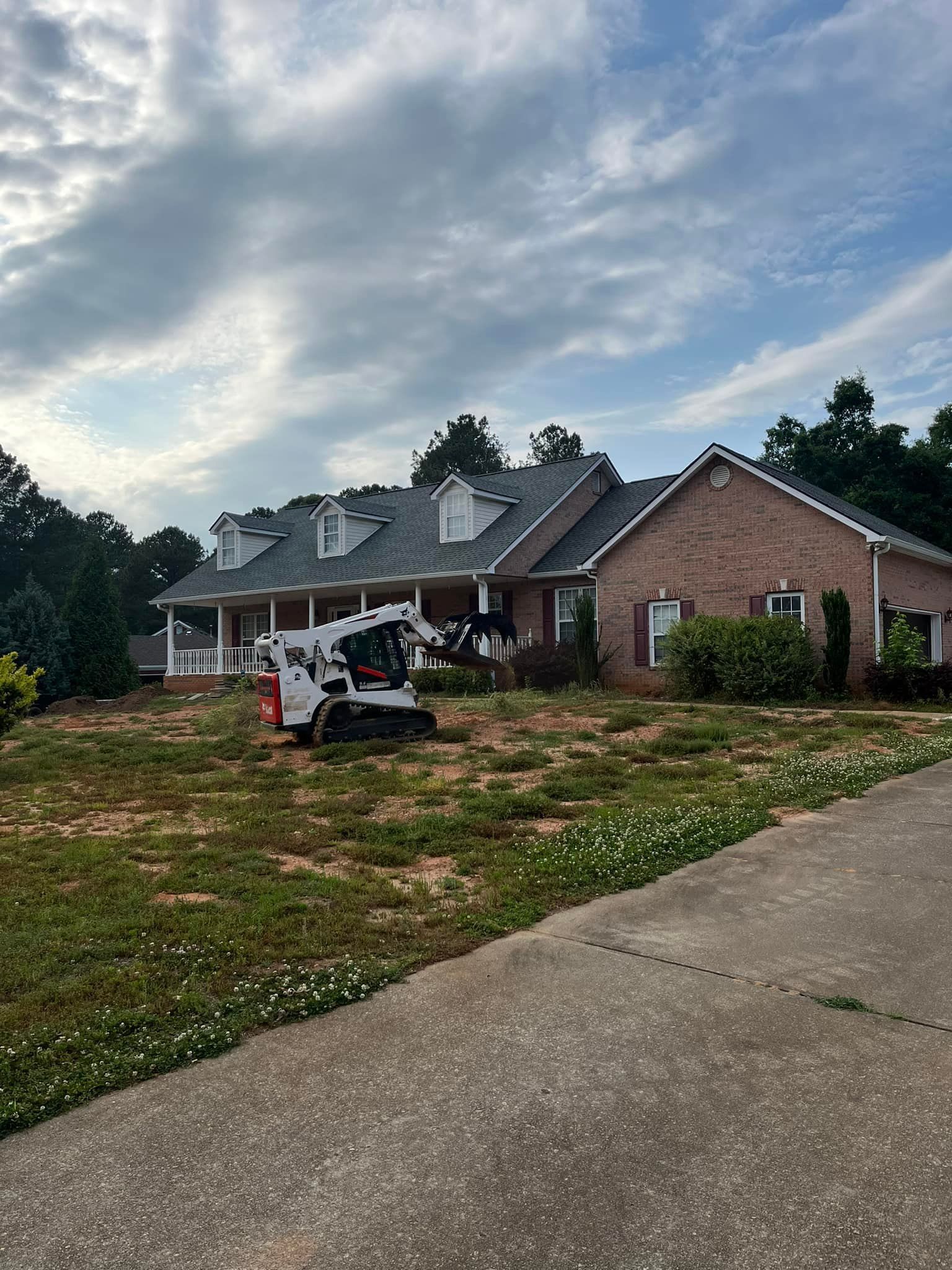 A bobcat is sitting in front of a large brick house.
