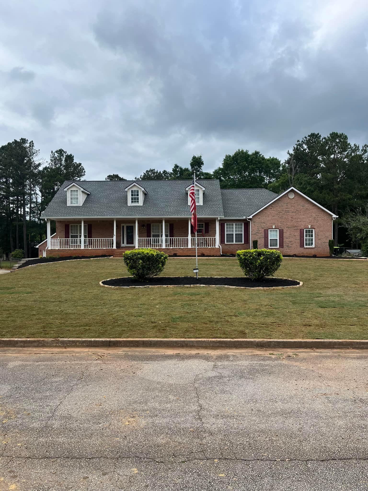 A large brick house with a porch and a flag in front of it.
