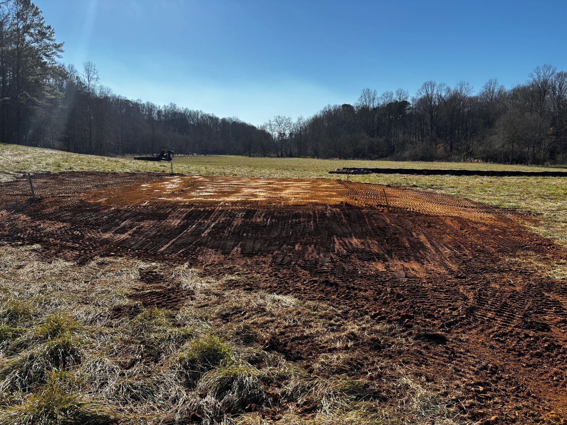 A dirt field with trees in the background and a blue sky