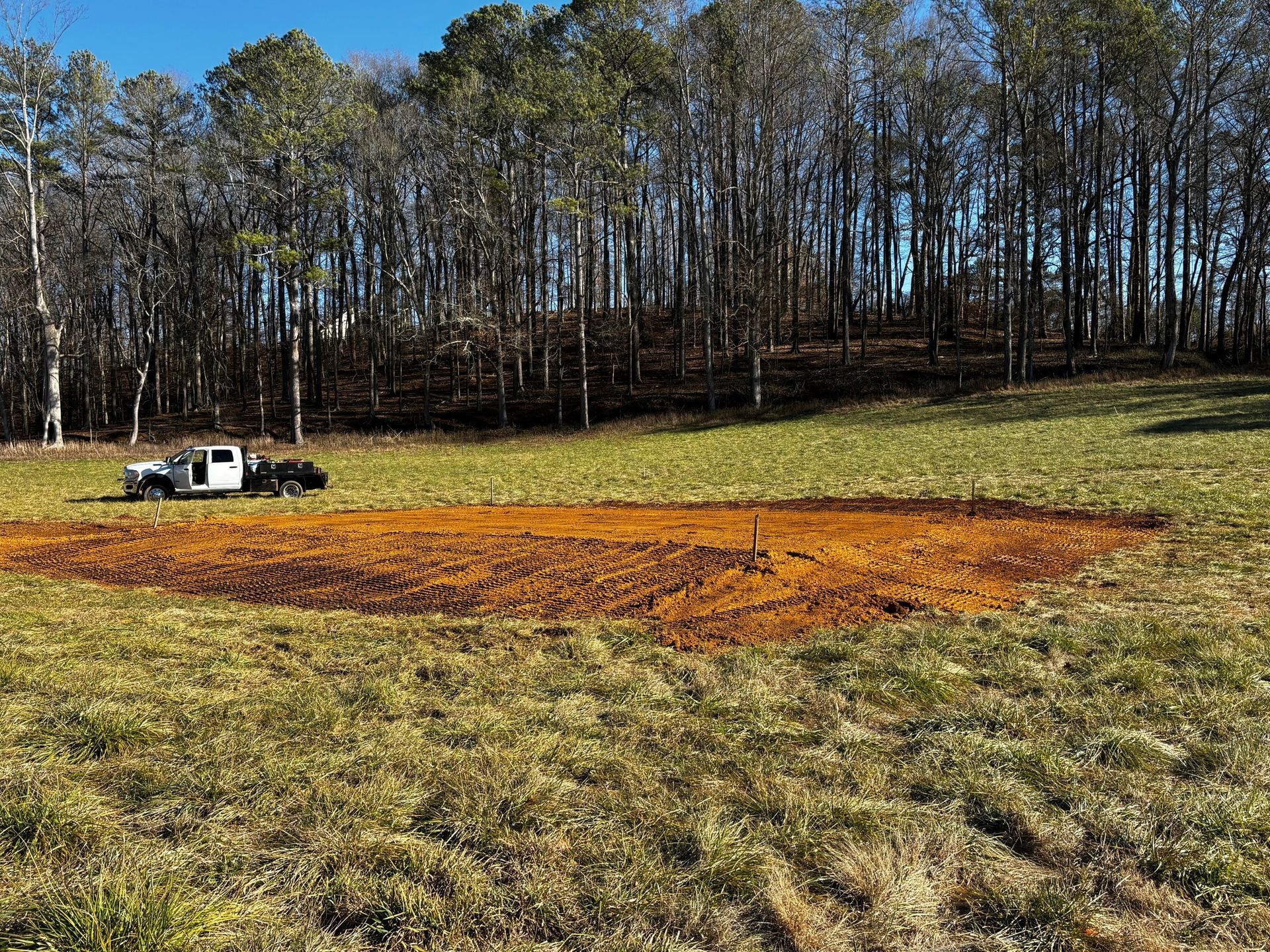 A white truck is parked in a field with trees in the background.